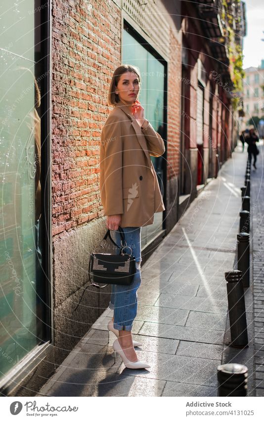 Stilvolles Modell mit Handtasche auf dem Bürgersteig im Tageslicht stehend Stoff elegant Kinn berühren Sonnenstrahlen schlank nachdenklich verträumt charmant