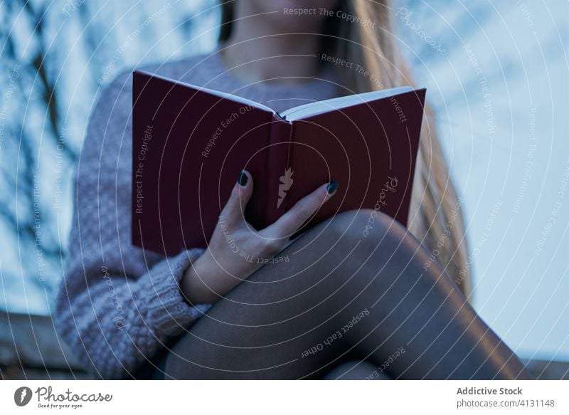 Nahaufnahme einer blondhaarigen Frau, die bei Sonnenuntergang im Park ein Buch liest ruhen abschließen anonym lesen Bank hölzern Frühling ernst Planer