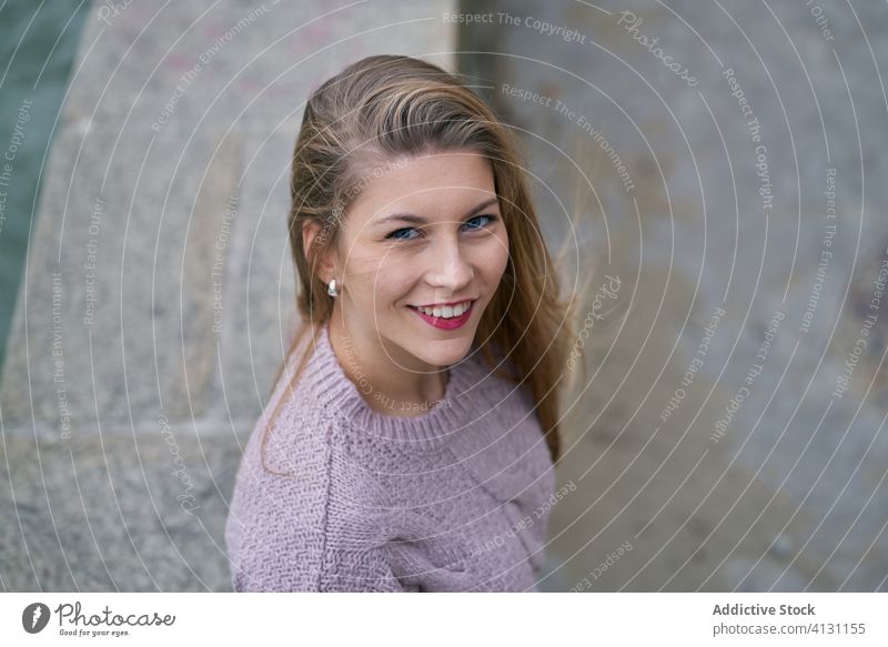 Junge Frau steht an einem Steinzaun und blickt in die Ferne, während der Fluss im Park zurückgeht Glück heiter Lächeln Herbst kalt friedlich Windstille