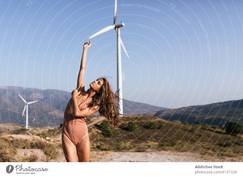 Zarte Frau tanzt allein in der Nähe des Windparks auf sonnigem Feld Tanzen Landschaft sinnlich Natur Ökologie schlank Stil hochreichen alternativ Windmühle