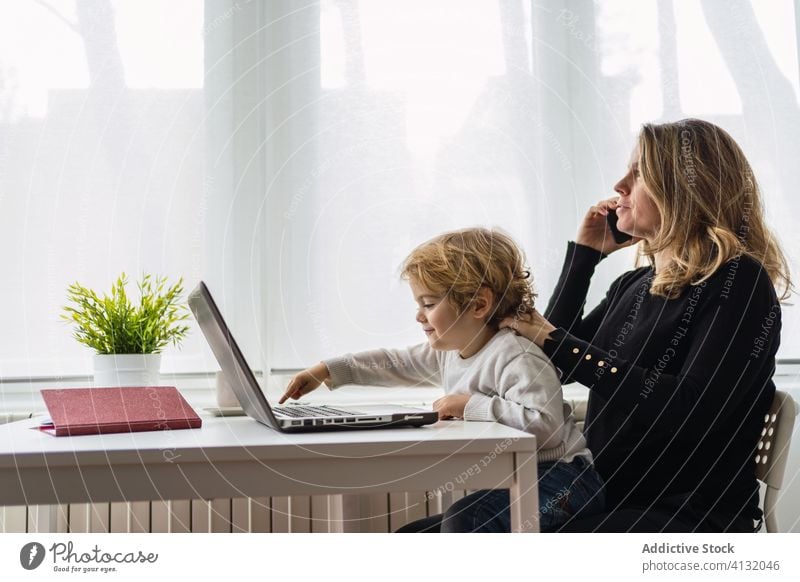 Frau mit kleinem Kind arbeitet zu Hause am Laptop Arbeit heimwärts Mutter benutzend Zusammensein online beschäftigt abgelegen neugierig Punkt Mutterschaft