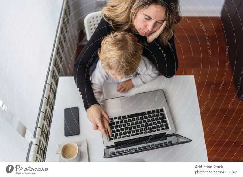 Frau mit kleinem Kind arbeitet zu Hause am Laptop Arbeit heimwärts Mutter benutzend Zusammensein online beschäftigt abgelegen neugierig Punkt Mutterschaft