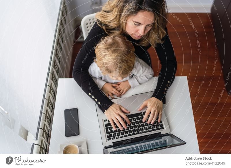 Frau mit kleinem Kind arbeitet zu Hause am Laptop Arbeit heimwärts Mutter benutzend Zusammensein online beschäftigt abgelegen neugierig Punkt Mutterschaft