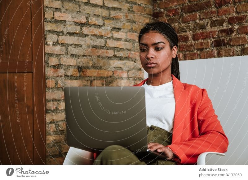 Moderne schwarze Frau mit Computer im Sessel Business Laptop online elegant Loft Design Fokus Innenbereich freiberuflich modern Gerät Apparatur Internet