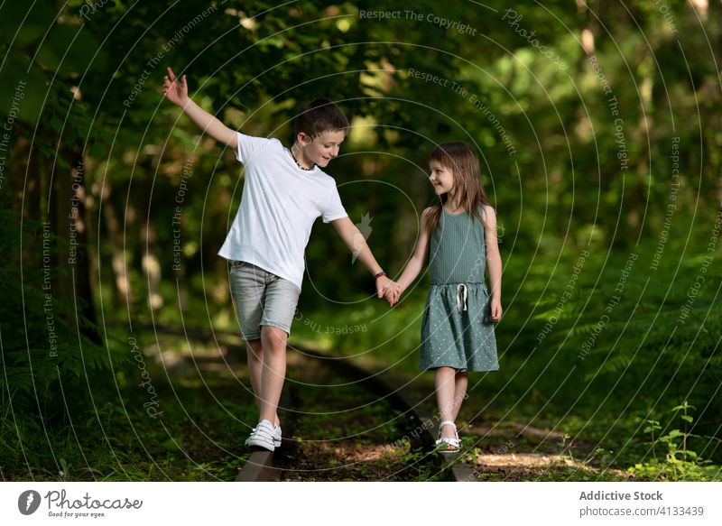 Zufriedene Kinder, die entlang einer stillgelegten Eisenbahnlinie im Park spazieren gehen Bruder Schwester Zusammensein freundlich Verlassen Schiene Spaziergang