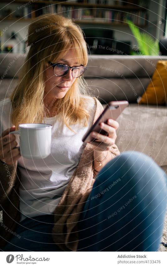 Lächelnde Frau, die sich auf Smartphone im Wohnzimmer selbstständig macht Selfie sich[Akk] entspannen unterhalten heimwärts Inhalt Foto benutzend weich Teppich