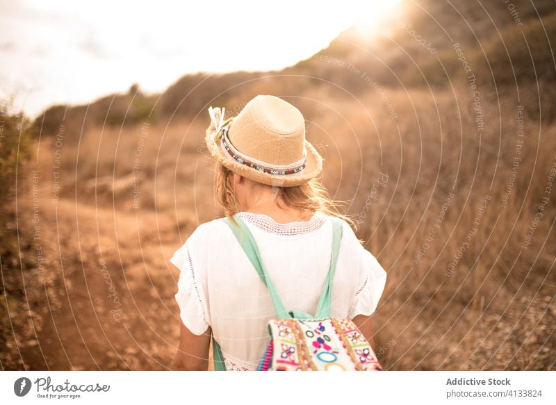 Reisende Frau, die bei Sonnenuntergang an einem Feld entlang läuft Hipster Reisender Urlaub Berge u. Gebirge Sommer Rucksack Natur levanzo Insel trocknen Gras