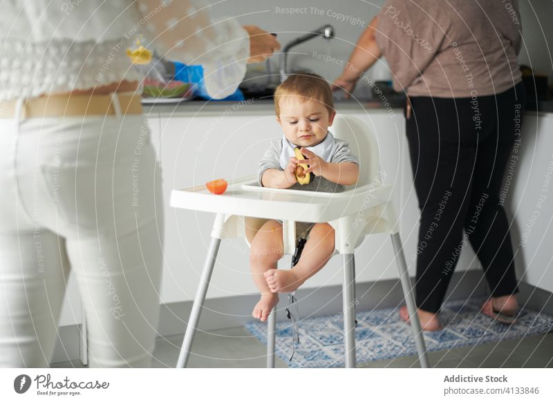 Kleines Baby sitzt im Hochstuhl und untersucht eine Avocado essen Stuhl Lebensmittel Küche heimwärts Kleinkind fokussiert untersuchen Kind niedlich Mahlzeit