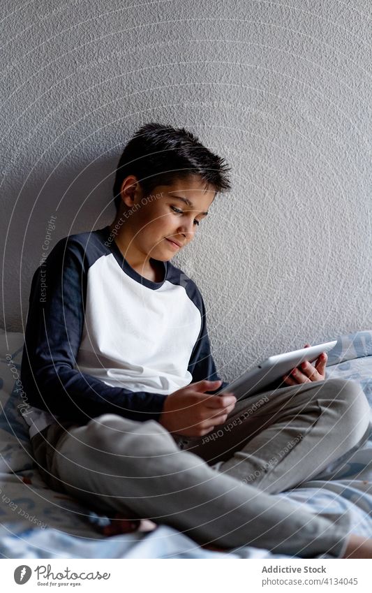 Entzückter Junge benutzt Tablette am Wochenende im Schlafzimmer Kind benutzend Decke Nacht zuschauend heiter Pyjama heimwärts bezaubernd Gerät Apparatur