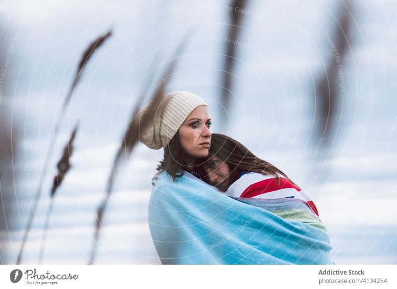 Junges lesbisches Paar, das sich mit der Flagge Großbritanniens umarmt Fahne Meeresufer wolkig Himmel Umarmung umhüllen Frauen Wegsehen Hut Lifestyle Umarmen