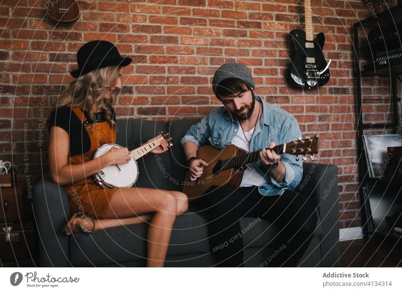 Fröhliches Paar, das auf dem Sofa sitzend Gitarre und Banjo spielt spielen banjo Musik Freizeit Duett Partnerschaft Freundschaft Zusammensein Beine gekreuzt