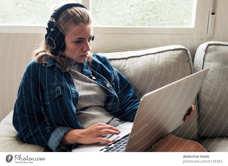 Moderne Frau, die zu Hause mit dem Laptop arbeitet heimwärts Kopfhörer Sofa benutzend Fokus Konzentration Arbeit jung lässig Drahtlos abgelegen Projekt