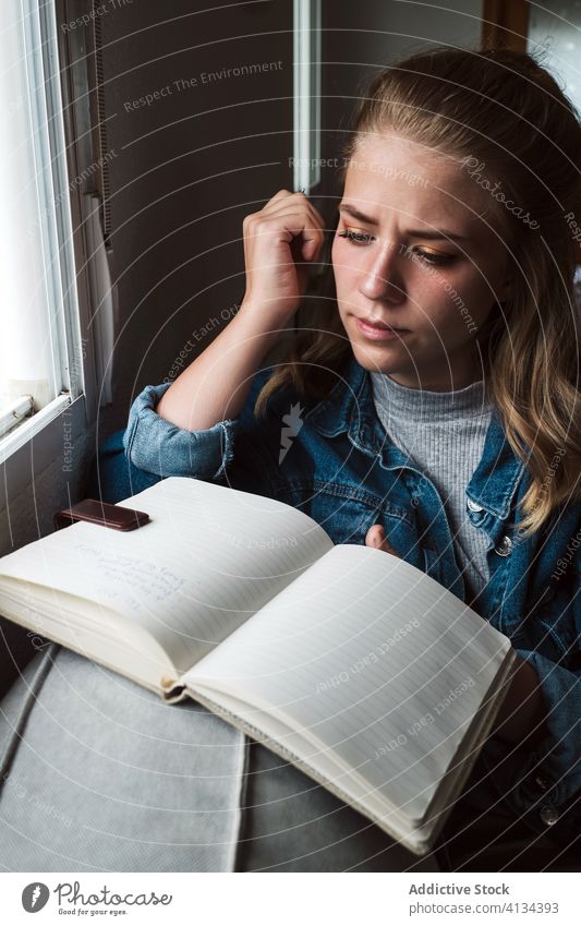 Nachdenkliche Frau mit Notebook am Fenster sitzend Tagebuch heimwärts besinnlich jung Schüler Notizblock nachdenklich lesen lässig Denken Windstille ruhig