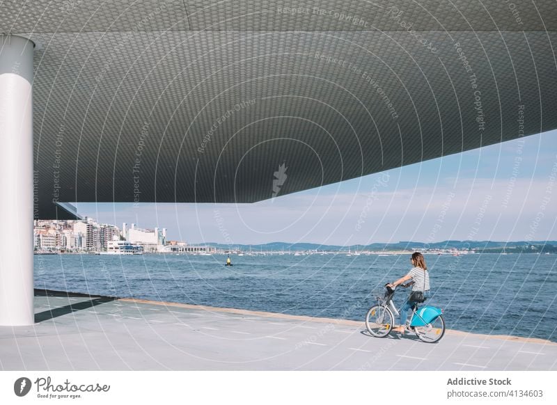 Frau fährt Fahrrad entlang der Strandpromenade Mitfahrgelegenheit Großstadt modern Gebäude Architektur sonnig Verkehr Hafengebiet Sommer Straße Zeitgenosse Stil