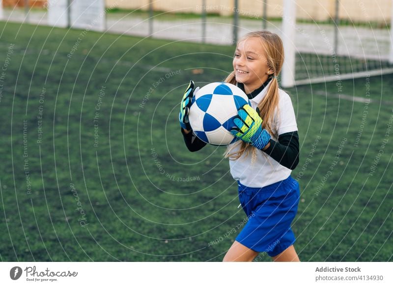 Glückliche junge Spielerin mit Ball in Fussballarena im Sportstadion Mädchen Fußball Feld Uniform Kind Club Kindheit Athlet Gerät Lächeln Schulmädchen heiter