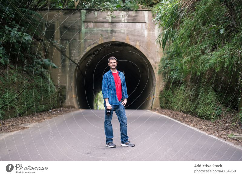 Männlicher Reisender in Jeans beim Fotografieren in der Nähe eines grünen Berges Tourist Fotoapparat fotografieren Straße Berge u. Gebirge Stollen Urlaub