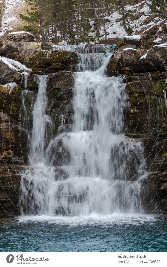 Wasserfall mit Pool zwischen schneebedeckten Bergen Berge u. Gebirge Schnee Wald Natur Landschaft Winter wild strömen malerisch Umwelt Felsen Harmonie kalt