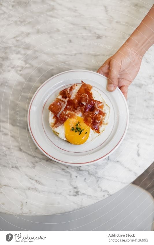 Person, die Bagel mit Ei und Schinken serviert Frühstück Prosciutto dienen Lebensmittel gebraten Ernährung geschmackvoll organisch frisch Morgen Mahlzeit