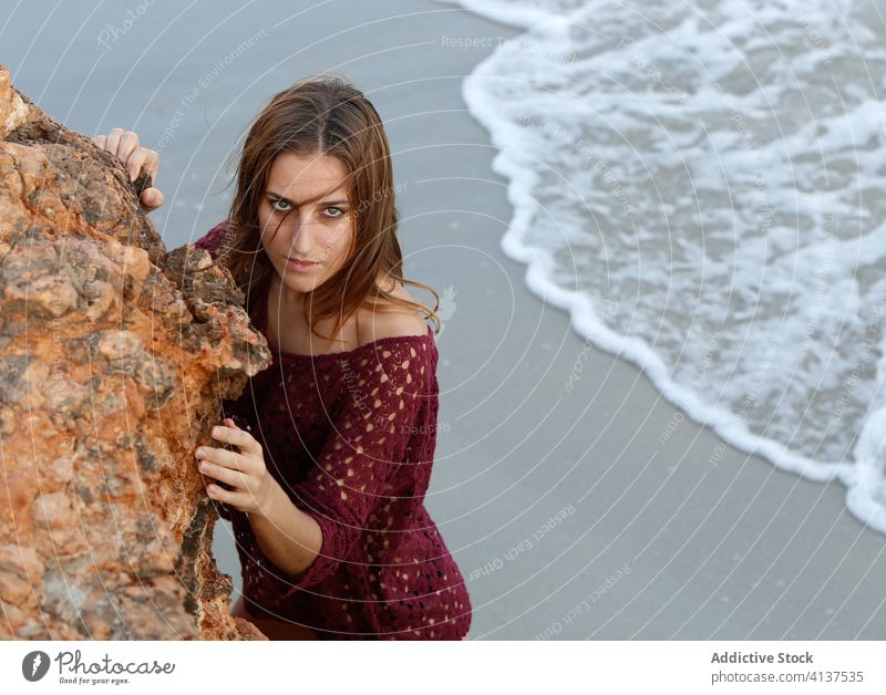 Ruhige Frau am Meeresufer in der Nähe eines Felsens Strand Bikini Feiertag Stein Windstille Sommer gestrickt Kleid emotionslos Urlaub Küste Ufer Sand stehen