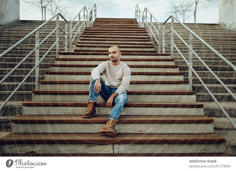 Inhalt stilvoller Mann sitzt auf einer Treppe in der Stadt Stil trendy Hipster modern Streetstyle Porträt jung Straße positiv Treppenhaus unrasiert Typ