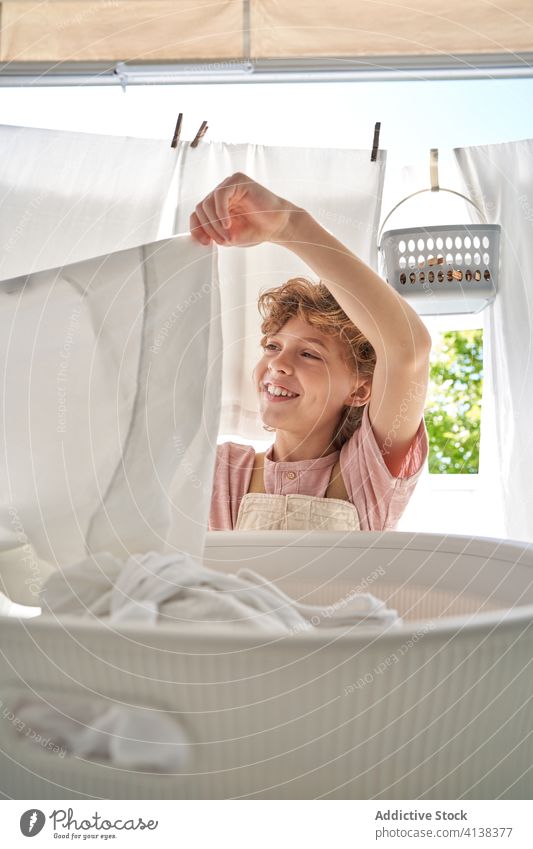 Kleiner Junge mit Korb voller Wäsche auf dem Balkon zu Hause Waschen Leinen heimwärts hängen Wäscherei heimisch Arbeit Kind Kindheit Hilfsbereitschaft sitzen