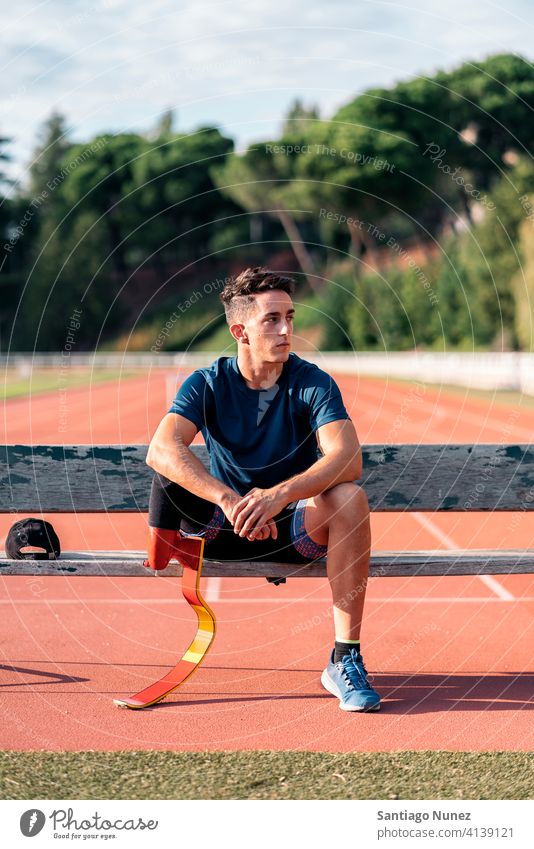 Behinderter Mann Athleten ausruhen Bank Sitzen Porträt Junge in die Kamera schauen Laufbahn Stadion jung Läufer Sport Prothesen Prothetik Behinderung