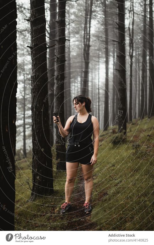 Weibliche Läuferin hört Musik im nebligen Wald zuhören Frau Smartphone müde Pause benutzend Training Wälder Nebel eng Sportkleidung Sportlerin Weg Gesundheit