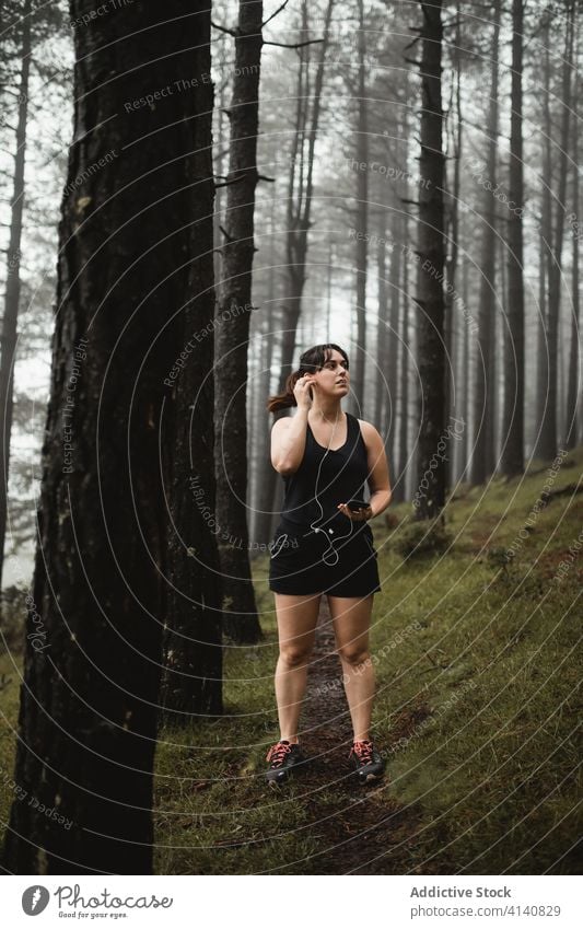 Weibliche Läuferin hört Musik im nebligen Wald zuhören Frau Smartphone müde Pause benutzend Training Wälder Nebel eng Sportkleidung Sportlerin Weg Gesundheit