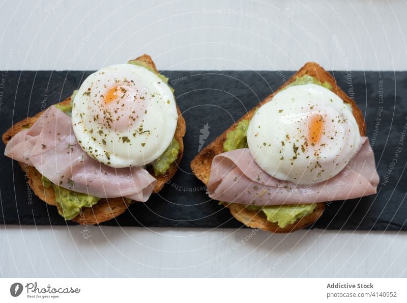 Toasts mit Schinken und Spiegeleiern auf Schiefertafel Zuprosten Frühstück Ei gebraten Holzplatte Guacamole geschmackvoll appetitlich gesunde Ernährung lecker