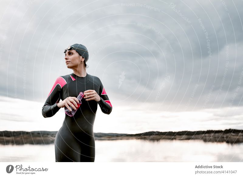 Erwachsene sportliche Frau im Tauchanzug am Ufer Neoprenanzug See Taucher Sport Flasche Natur Inspiration Sonnenuntergang Barfuß Getränk Badeanzug trinken