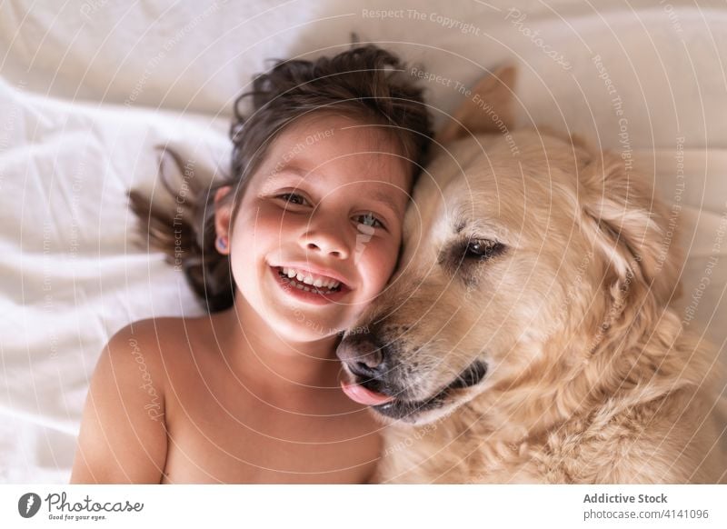 Glückliches Mädchen liegt mit Hund auf zerknittertem Bettlaken ruhen Zuneigung Begleiter Zahnfarbenes Lächeln Zusammensein idyllisch heimwärts Harmonie Schot