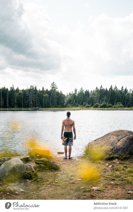 Mann schleift in der Nähe des Flusses und schaut weg Stein Ufer reisen Windstille Himmel wolkig Nationalpark la mauricie Quebec Kanada Küste Natur Gelassenheit