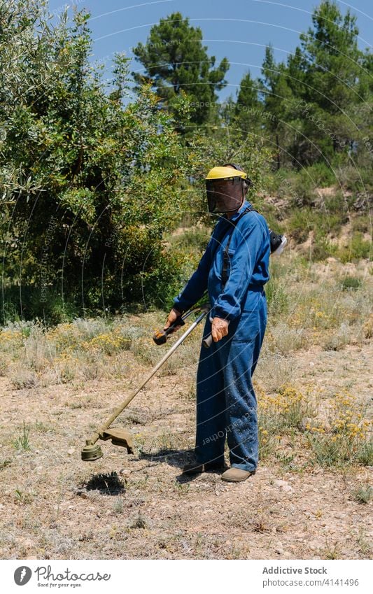 Mann in Uniform mit Grasschneider im Garten Kutter Bürste mähen sonnig Rasen behüten männlich Werkzeug professionell Schutzhelm Arbeiter Gerät Sicherheit Job