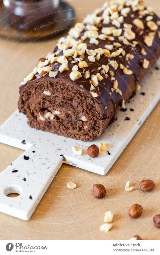 Schweizer Rollkuchen auf Schneidebrett auf Tisch Schweizer Brötchen Kuchen lecker Dessert süß Schokolade Glasur Haselnuss selbstgemacht rollen geschmackvoll