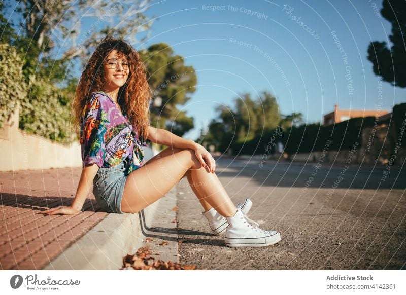 Wunderschöne Frau sitzt auf Asphalt Straße Zahnfarbenes Lächeln Augen geschlossen Glück Lifestyle aufgeregt Harmonie Blauer Himmel sorgenfrei Baum heiter