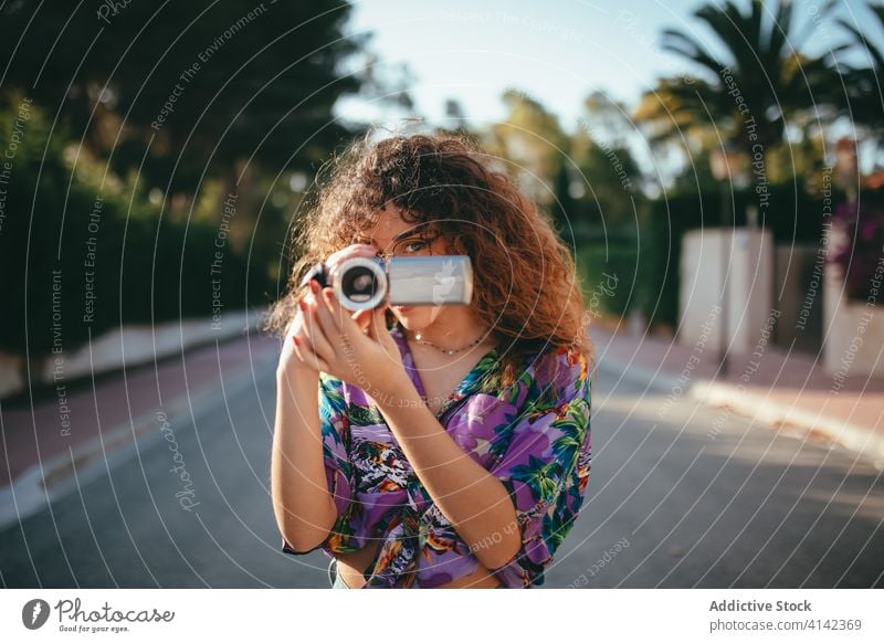 Fröhliche Frau mit Videokamera auf der Straße im Sommer Fotokamera Aufzeichnen Zahnfarbenes Lächeln Hobby Blauer Himmel benutzend Gerät Camcorder Glück