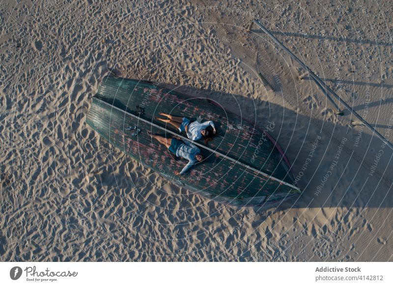 Entspanntes Paar, das sich auf einem umgestürzten Ruderboot am Strand ausruht sich[Akk] entspannen ruhen lässig hölzern auf den Kopf gestellt Sand romantisch