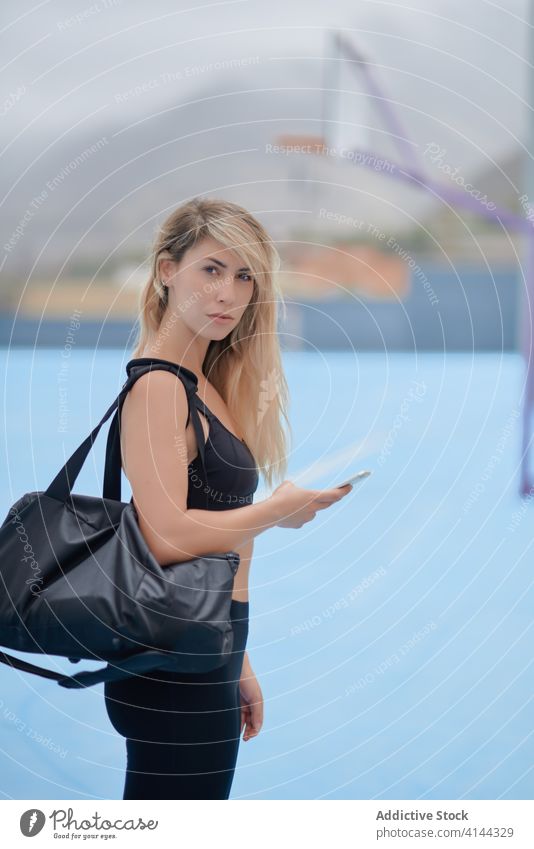 Gut gelaunte, fitte Frau, die auf einem Sportplatz ihr Smartphone benutzt passen sportlich benutzend Lächeln Glück Sportpark Sportlerin Athlet Pause Nachricht