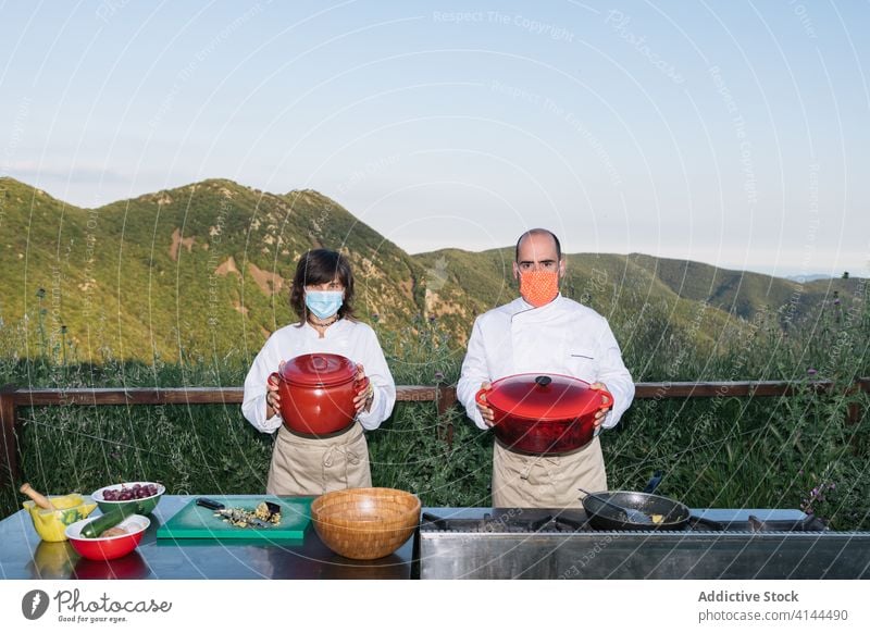 Köche in Schürzen mit zubereiteten Gerichten auf dem Lande Mann Frau Küchenchef Landschaft Berge u. Gebirge Gelände Kochtopf vorbereiten professionell Job