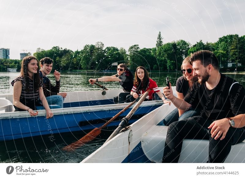 Glückliche Freunde, die sich auf Booten vergnügen und ihr Smartphone benutzen Teich benutzend Lachen positiv Natur Freundschaft Aktivität malerisch Browsen jung