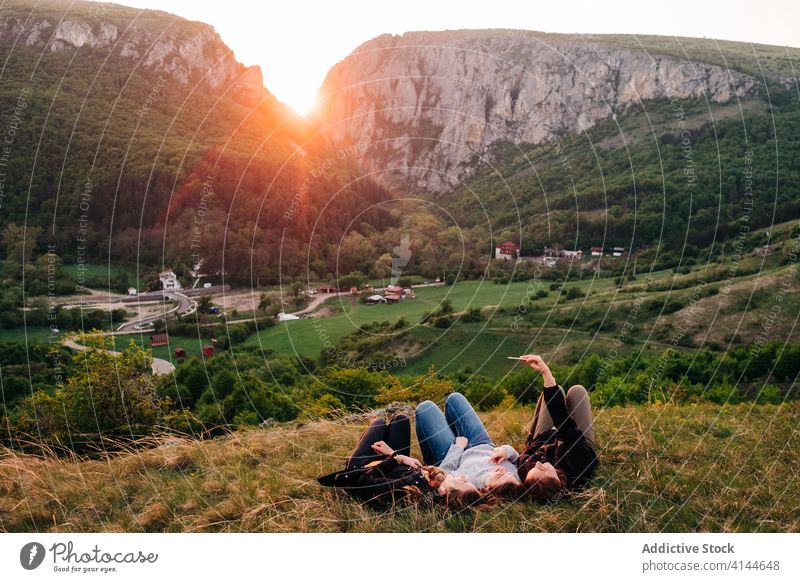 Freunde im Gras liegend in bergigem Gebiet Selfie Zusammensein Berge u. Gebirge sich[Akk] entspannen Sonnenuntergang Smartphone benutzend freundlich Unternehmen