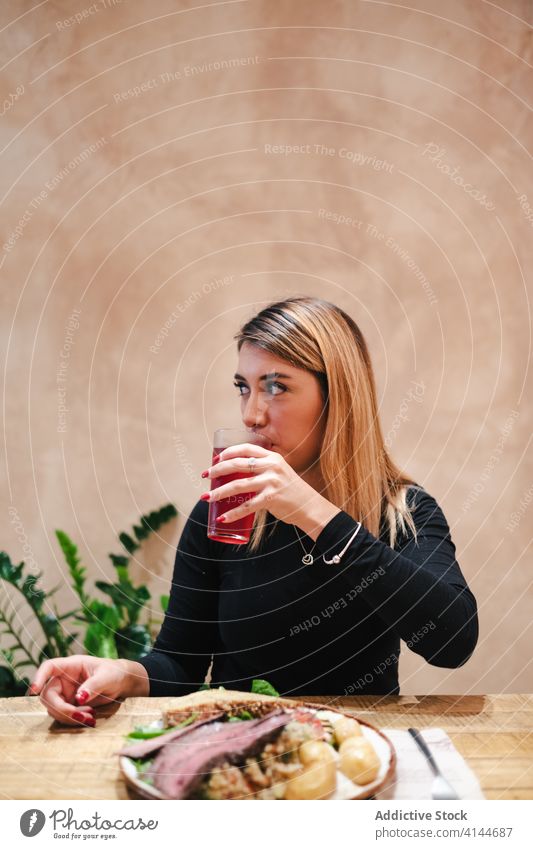 Zufriedene Frau trinkt Saft und sitzt am Tisch in einem Café trinken geschmackvoll Rindfleisch lecker Getränk dine positiv Mittagessen Mahlzeit Abendessen Küche