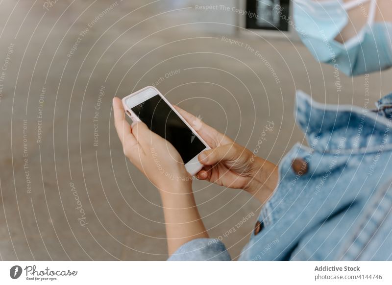 Frau mit Schutzmaske benutzt Smartphone auf der Straße benutzend Mundschutz Browsen Telefon Mobile modern urban Gerät Apparatur COVID COVID19 Coronavirus