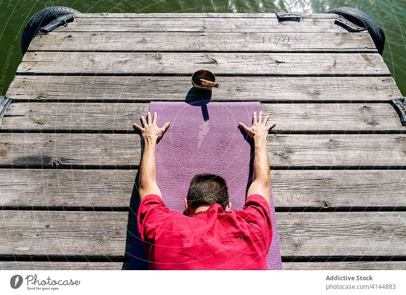 Gesichtsloser Mann, der seinen Körper streckt, während er die Yogahaltung Utthita Balasana auf einem Steg einnimmt erweitertes Kind Erholung Windstille Dehnung