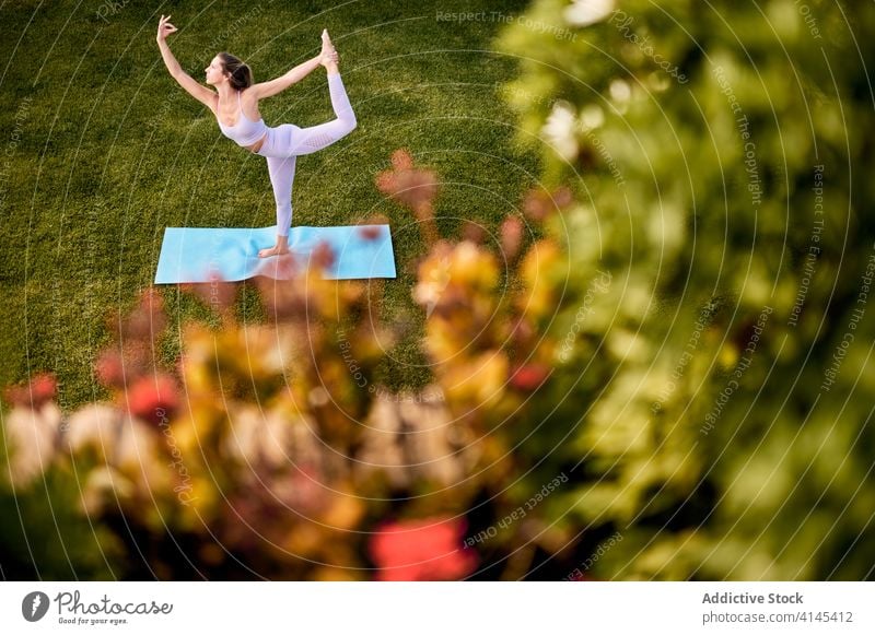 Anmutige Frau beim Yoga in Lord of the Dance-Pose Herr der Tanzpose Natarajasana beweglich Sportbekleidung Rasen Park ruhig Mudra gestikulieren grün Gesundheit