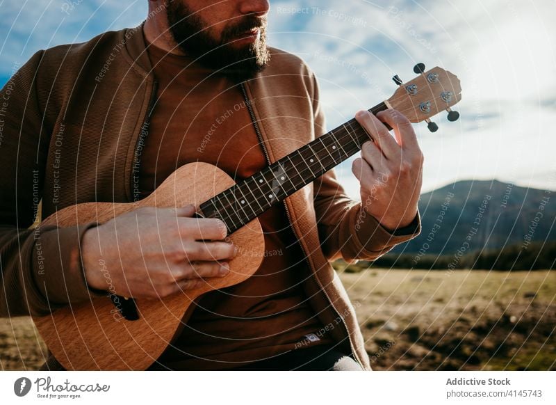 Anonymer bärtiger Mann spielt Ukulele auf dem Lande spielen Landschaft Zaun Himmel wolkig Musik puerto de la morcuera Spanien männlich reisen Urlaub Ausflug