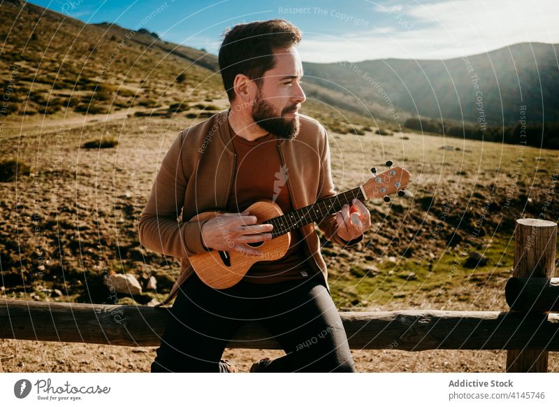 Bärtiger Mann spielt Ukulele auf dem Lande spielen Landschaft Zaun Himmel wolkig Musik puerto de la morcuera Spanien männlich reisen ernst Urlaub Ausflug Natur