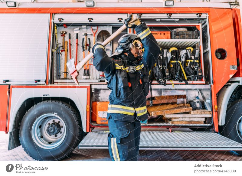 Anonymer Feuerwehrmann mit alter Spitzhacke in der Nähe eines Feuerwehrwagens führen Uniform Gerät Pickel Lastwagen Werkzeug Arbeit Sicherheit Weste Instrument