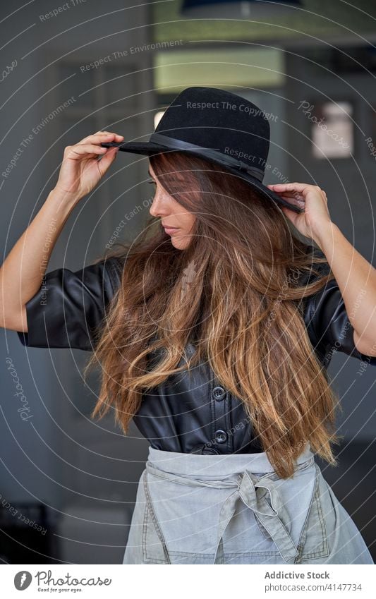 Selbstbewusste junge Frau in trendigem Outfit selbstbewusst Stil trendy Hut Porträt modern lange Haare nachdenklich Mode urban elegant Zeitgenosse Lächeln