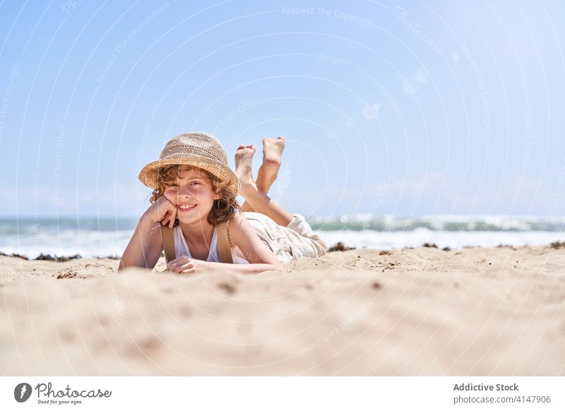 Lächelnder Junge auf sandigem Mantel in den Sommerferien niedlich Lügen Stützenkinn ruhen Meeresufer Strand Barfuß Resort sorgenfrei Seeküste Urlaub wenig Küste